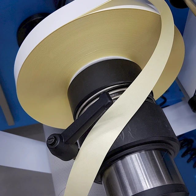 Cream adhesive tape unwinding from roll on mandrel