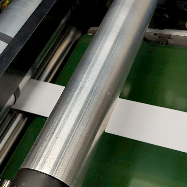 White strip on green conveyor under steel rollers